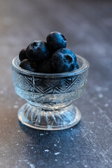 Fresh blueberries overflowing a crystal glass bowl on a dark textured surface