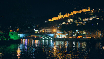 Illuminated Narikala fortress and enlightened embankment reflect in water of Kura river. Lights of Tbilisi at night © Philipp Berezhnoy
