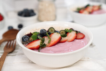 Presented by fruits putting yogurt toppings with strawberry, berry, oats, raisins and chia seed decorated by peppermint in white blow. Pink background. Set of healthy dairy product choice. Pecuniary.