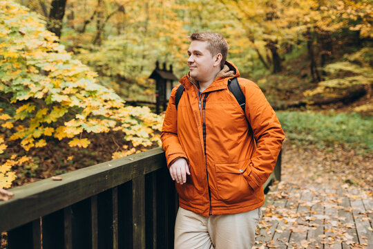 30s Plus size male with backpack smiling outside on an adventure. Hiking, lifestyle, adventure and tourism concept. Young man standing on the bridge in woodland, autumn time.