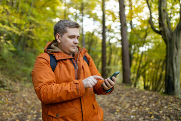 Young Caucasian 30s man backpacker with smartphone catching signal at wooden forest. Road trip, transport, travel, technology and people concept. High quality photo