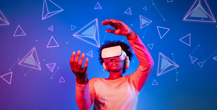 Fototapeta African girl with VR glasses standing at blue and pink background and looking at floating geometric shape. Excited person searching and entering visual reality world. Technology innovation. Ingenuity.