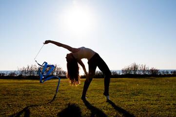 Rhythmic gymnast performing yoga. Sport flexibility. Gymnast hold ribbon in backlit. Gymnastics...
