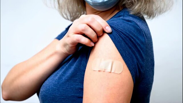 Vaccinated woman showing shoulder after vaccine getting, plaster on arm of person, concept of people and mask. 