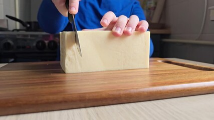 Close-up of hands cutting cheese on kitchen counter, child or adult struggles to cut large piece of cheddar. Video tutorial or recipe for cooking at home