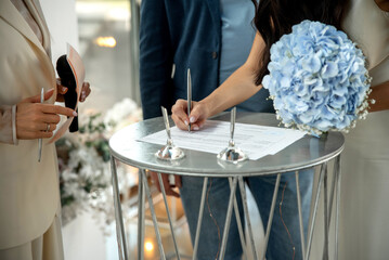 A bride signs wedding documents on a round metal table with witnesses
