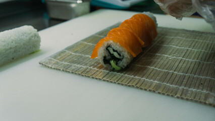 The chef prepares a Philadelphia sushi roll with vibrant red fish on top and creamy cheese filling,...