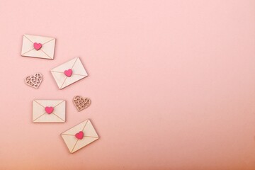 A pink background with several small, wooden small envelopes topped with a pink heart decorated...
