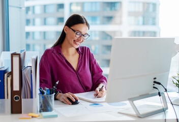 Successful business career. Happy businesswoman taking notes while working with computer in office,...