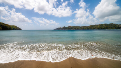 Gentle waves roll onto the sandy beach at Kings Bay ,crystal-clear turquoise water, the vast horizon and soft clouds create a peaceful, untouched tropical paradise. Tobago , Caribbean sea. Copy space