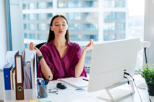 Coping with stress at work. Woman office worker meditating at workplace in office, doing breathing exercises with closed eyes