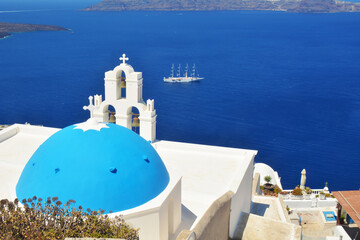 Fototapeta premium Fira capital of Santorini island, Cyclades islands Aegean sea, Greece. Panoramic view of caldera, with blue dome and tower bell in the foreground. 