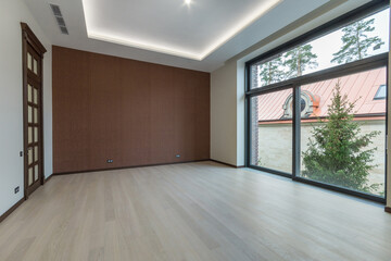 An empty room with a panoramic window in a luxurious mansion. Light laminate, brown door with glass windows. Unfurnished.