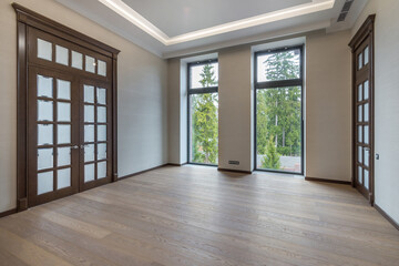 Beautiful decoration of the premises of a luxurious mansion. Dark doors with frosted glass windows, panoramic windows overlooking the forest. Unfurnished.