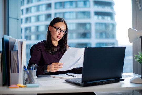 Focused woman secretary accountant working with documents, checking financial reports at workplace in office