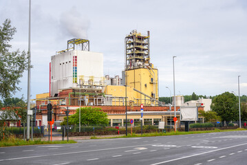 View of an manufacturing plant with chimneys belching out white smoke in suburban industrial park on a cloudy day