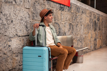 latin Tourist waiting for train sitting on bench holding suitcase