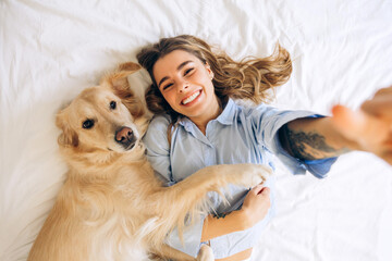 Smiling woman taking a selfie with golden retriever on bed