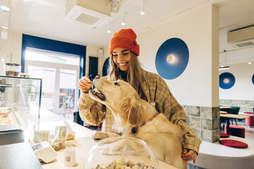Woman giving treat to golden retriever in coffee shop