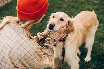 Woman wearing orange beanie gently holding face of golden retriever dog