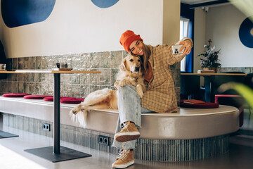 Woman taking selfie with golden retriever in modern cafe