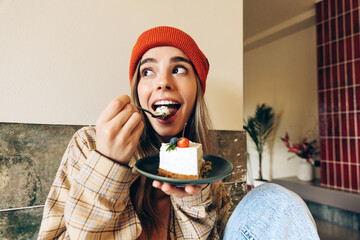 Cheerful young woman eating cheesecake in a cafe