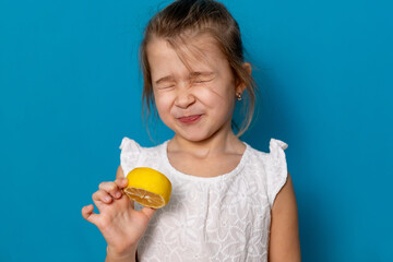 Funny little child girl try to taste fresh lemon, wrinkles and makes a grimace. Sour taste, facial...