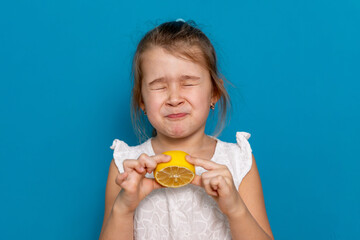 Funny little child girl try to taste fresh lemon, wrinkles and makes a grimace. Sour taste, facial...