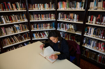 A focused individual immersed in a book at a table within a cozy library space.