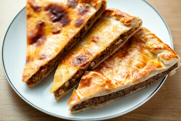 Three slices of traditional Russian meat pies served on a white plate The pies have a golden brown crust and are filled with minced meat