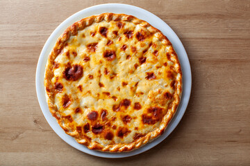 Golden brown traditional Russian pie displayed on a white plate against a wooden table background