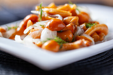 Close-up of marinated mushrooms with slices of onion and dill on a white plate