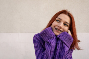 Smiling Redhead Girl with Braces Wearing a Purple Knitted Sweater	