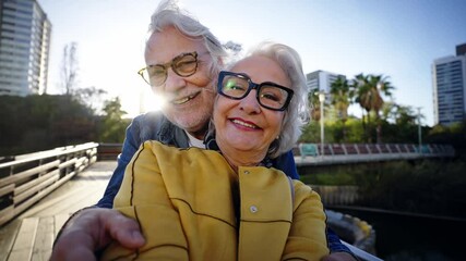 Portrait of happy senior couple taking selfie outdoors in a park of the city. Smiling elderly people in love traveling together on vacation. Cheerful grandparents posing for photo with mobile phone. - Powered by Adobe