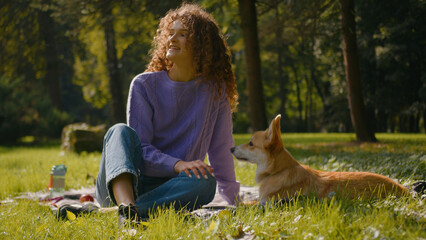 Caucasian young woman girl playing with cute little friend dog welsh corgi on grass outdoors female handler pet owner stroking puppy relaxing in city park nature human and domestic animal friendship