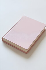 Fototapeta premium A closed pink notebook rests on a white surface. Simple, elegant, and ready for your notes or ideas.