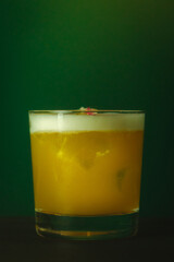 Vibrant Yellow Cocktail with Foam in Lowball Glass Refreshing Drink Against a Lush Green Backdrop