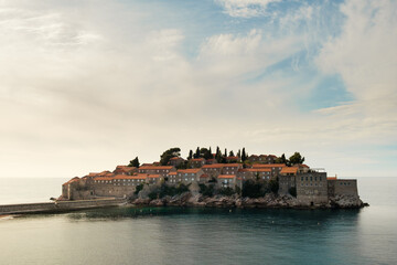 Naklejka premium Sveti Stefan island with pebble beach and medieval Mediterranean fishing village at sunrise
