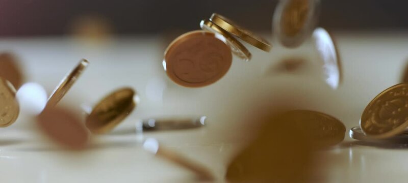 Super of slow-motion shot of a pile of golden Euro coins falling down from above. Close-up view