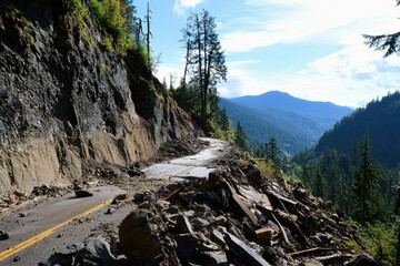 A destructive landslide burying a mountain road, with rocks and debris tumbling down the slope.