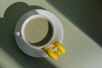 Green latte matcha with yellow macaron dessert on pastel background with creative deep shadows....