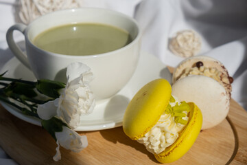 Nutrient-rich matcha drink with trendy macaron dessert on wooden tray in bed with fresh flowers. Morning beautiful breakfast present gift idea. Vibrant creative colors. Natural energy givers tea