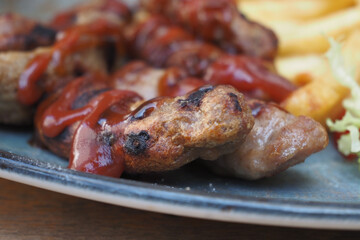 Grilled Meat With Ketchup Served Alongside Fries and Leafy Salad