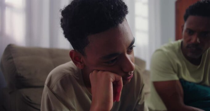 Teenage son showing disinterest and boredom during a conversation, father sitting nearby with a serious expression, highlighting generational conflict and family tension