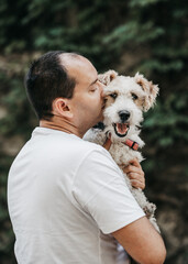 Bald man in a white t-shirt kissing a fox terrier dog. The dog, mouth open and tongue out, love for dogs happiness.