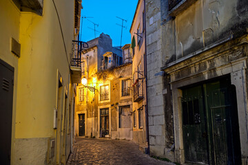 Obraz premium A narrow, illuminated hillside alley at night in the historic medieval Alfama district of Lisbon, Portugal.
