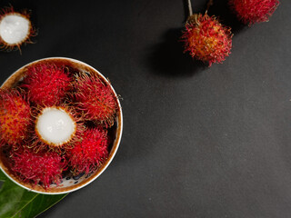 sweet and fresh tropical fruit rambutan sitting on a wooden base on a black background with copy space © Arsyah Studio