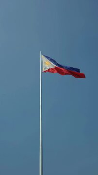 Philippine flag waving in the wind against a blue sky background. Vertical 4K footage