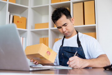 Focused entrepreneur writing notes while holding package in small business startup for e-commerce...