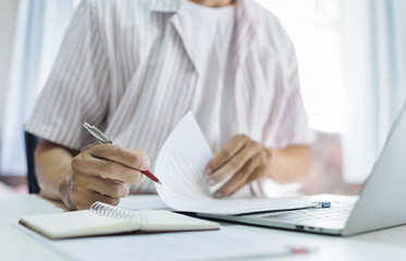 Asian man in casual clothes sitting at desk and using laptop working at home, freelancer working online and doing part time job at home